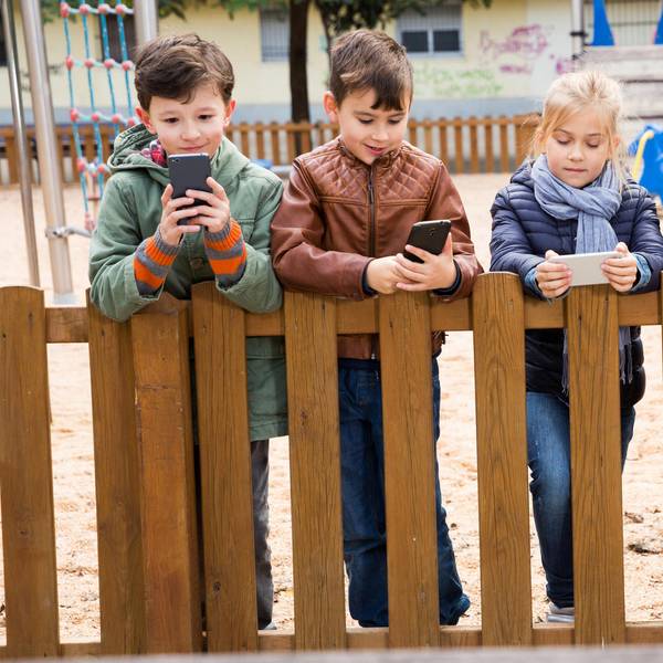 Grundschulkinder stehen mit Handys an einem Zaun.