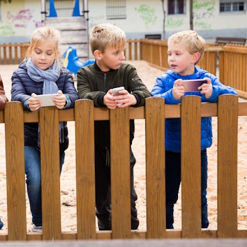 Grundschulkinder stehen mit Handys an einem Zaun.